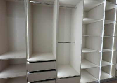 Nyitott fehér gardróbszekrény polcokkal és ruhatartóval