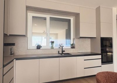 Fehér konyhabútor fekete munkapulttal és ablak alatti mosogatóval